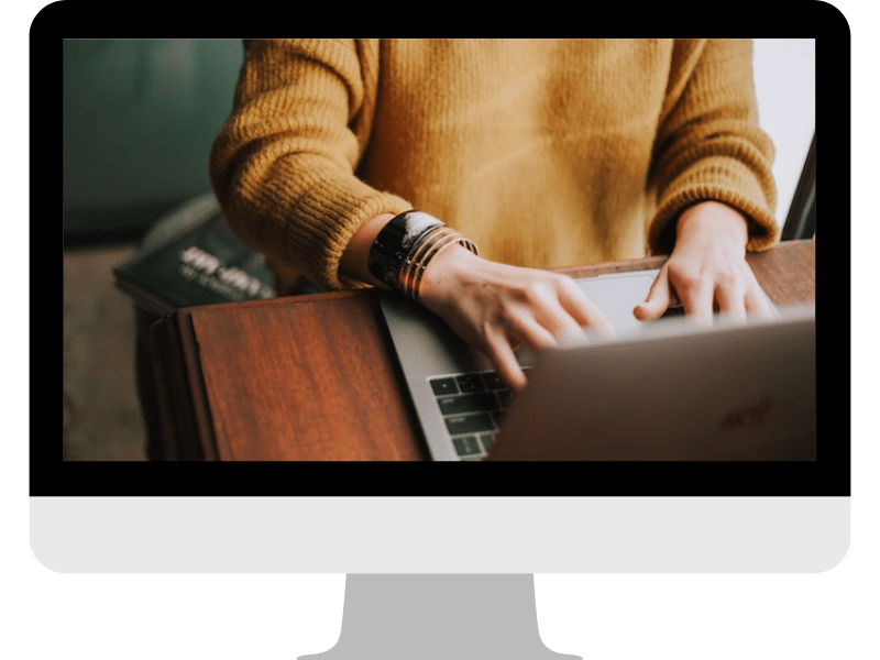 A woman in a yellow sweater typing on her laptop computer.